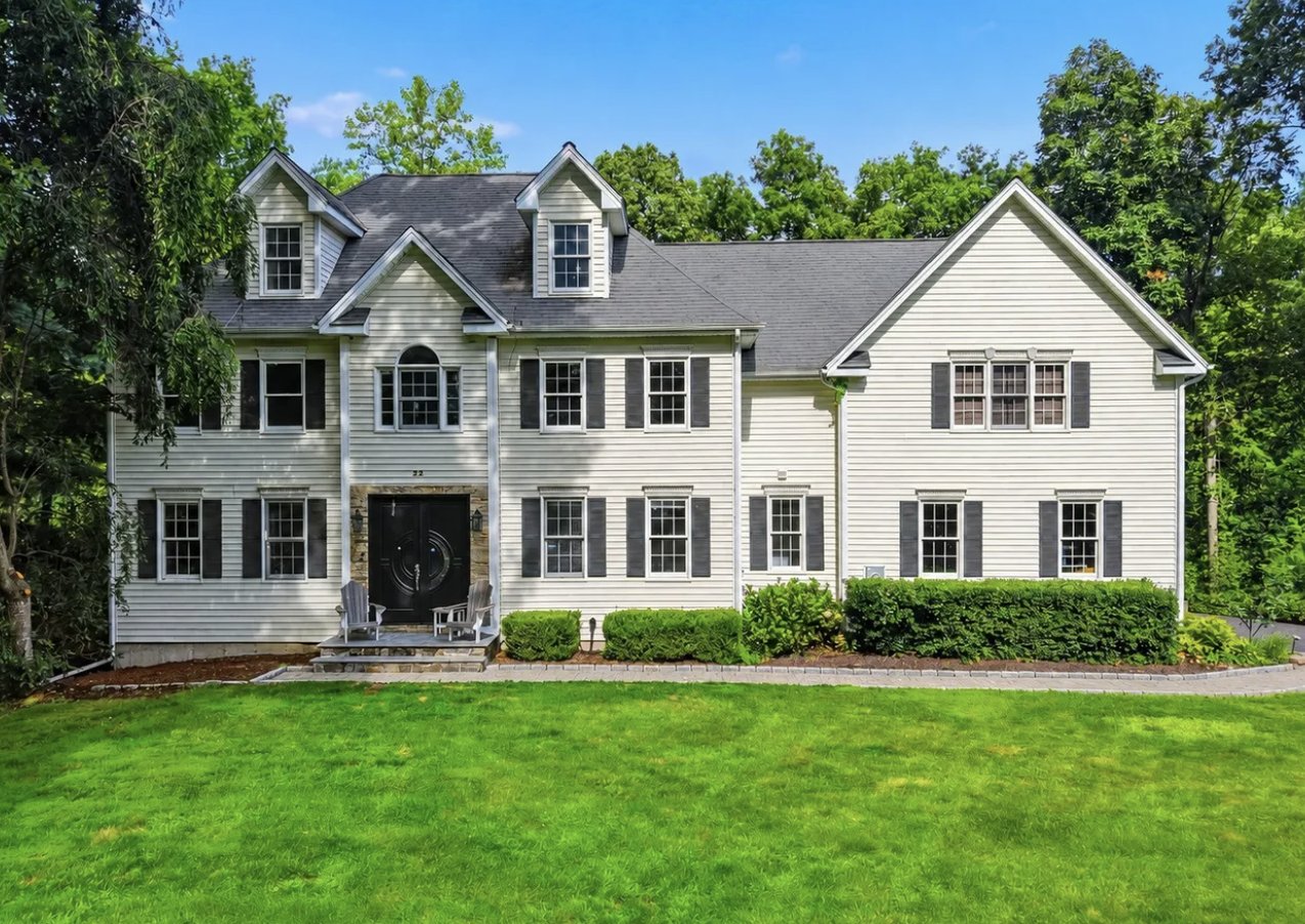 22 Morehouse Lane, Norwalk CT, a white Colonial home with black shutters on a landscaped lot, listed at $1,099,000